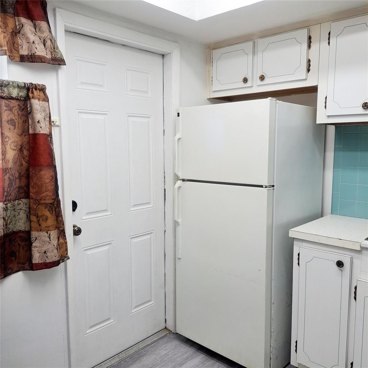 A kitchen features a white refrigerator, white cabinets, a blue tiled backsplash, and a door — 6730 Arbor Drive # 210, Miramar FL 33023, MIRAMAR, FL