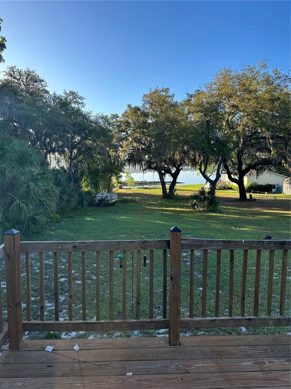 A wooden deck overlooks a grassy backyard with large trees and a view of water — 212 ASHLEY STREET, HAWTHORNE, FL