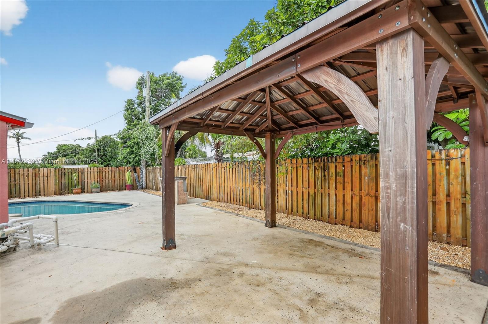 A wooden gazebo stands on a concrete patio next to a swimming pool and fence — 2681 NW 63rd Ave, Margate FL 33063, MARGATE, FL