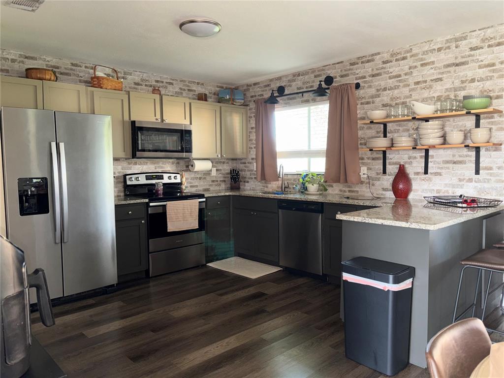 A kitchen features two-toned cabinetry, stainless steel appliances, open shelving, and a brick-patterned backsplash — 6866 KAPPA PLACE, NORTH PORT, FL