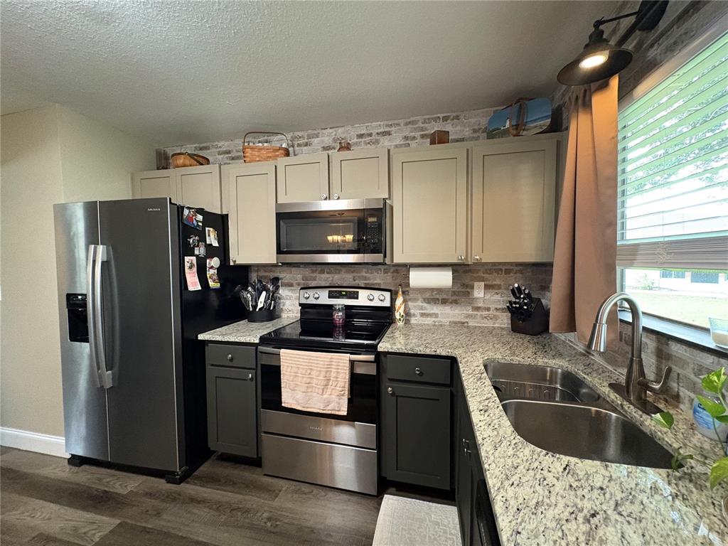 A kitchen features two-toned cabinets, stainless steel appliances, granite countertops, and a faux brick backsplash — 6866 KAPPA PLACE, NORTH PORT, FL