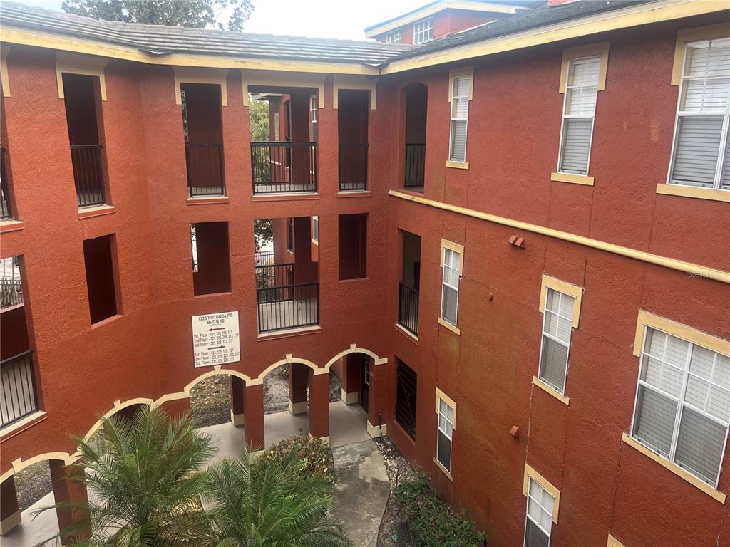 An exterior view of a multi-story, red-stucco apartment building with open-air walkways and balconies — 1325 ROTONDA POINT UNIT 313, LAKE MARY, FL