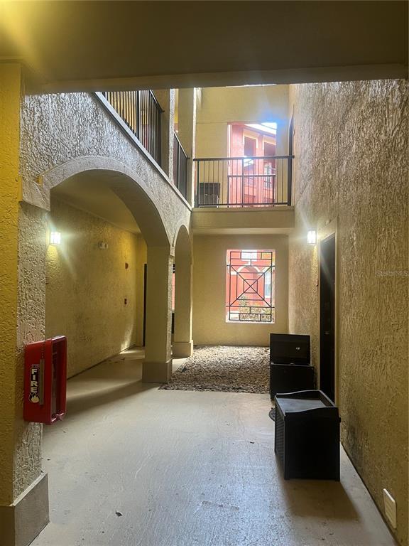 An outdoor covered walkway features stucco walls, arched openings, a gravel patch, and metal railings — 1325 ROTONDA POINT UNIT 313, LAKE MARY, FL