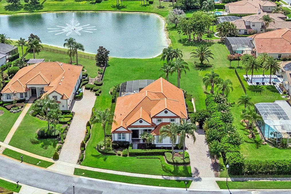 An aerial view shows two houses with orange tile roofs near a pond with a fountain — 5746 OXFORD MOOR BOULEVARD, WINDERMERE, FL