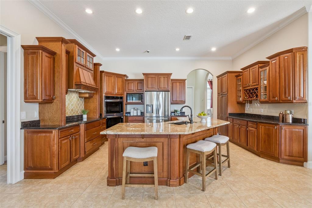 A kitchen features wood cabinets, granite countertops, a central island with seating, and tile flooring — 5746 OXFORD MOOR BOULEVARD, WINDERMERE, FL