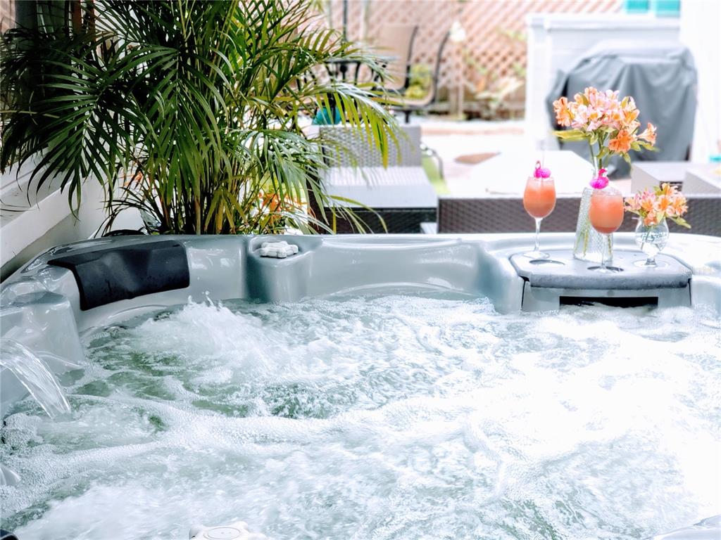 A bubbling hot tub sits on a patio with tropical plants and two cocktail glasses — 2035 28TH AVENUE N UNIT 1/2, ST PETERSBURG, FL