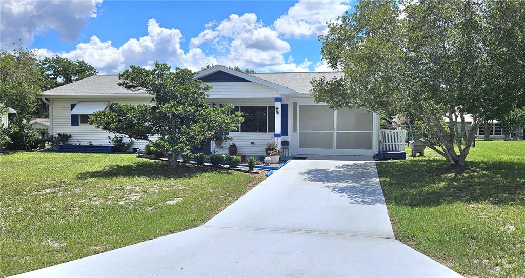 A single-story house with white siding, blue shutters, and a concrete driveway under a cloudy sky — 10957 SW 79TH TERRACE, OCALA, FL