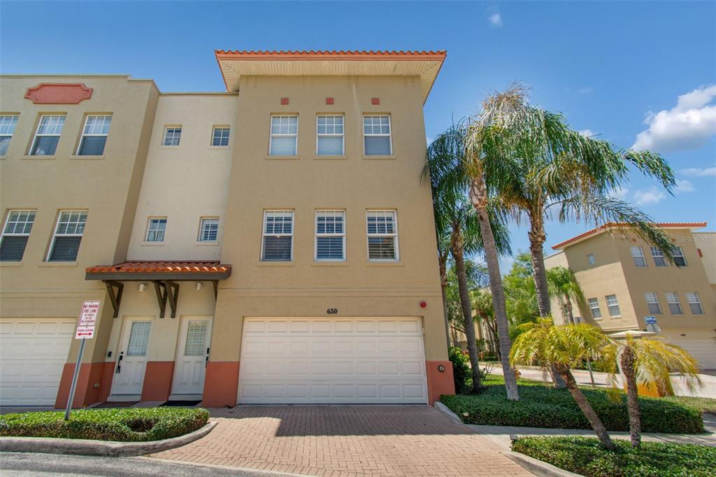 A three-story townhouse with a beige stucco exterior, a two-car garage, and palm trees — 650 SIREN WIND LANE, CLEARWATER, FL