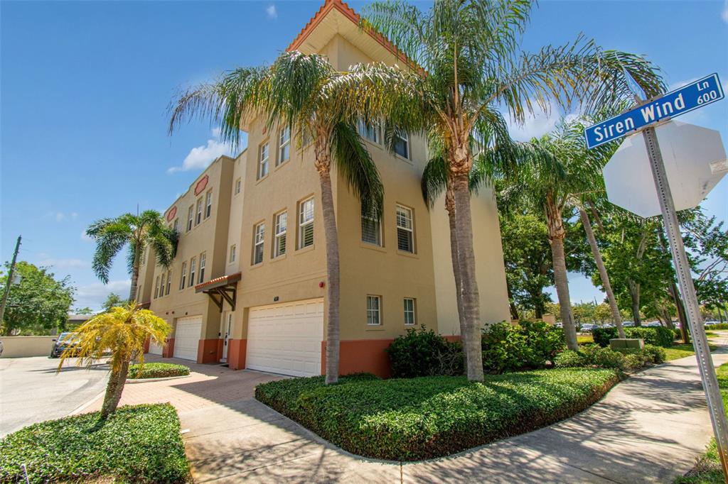 A three-story tan stucco townhouse with a two-car garage and palm trees in front — 650 SIREN WIND LANE, CLEARWATER, FL
