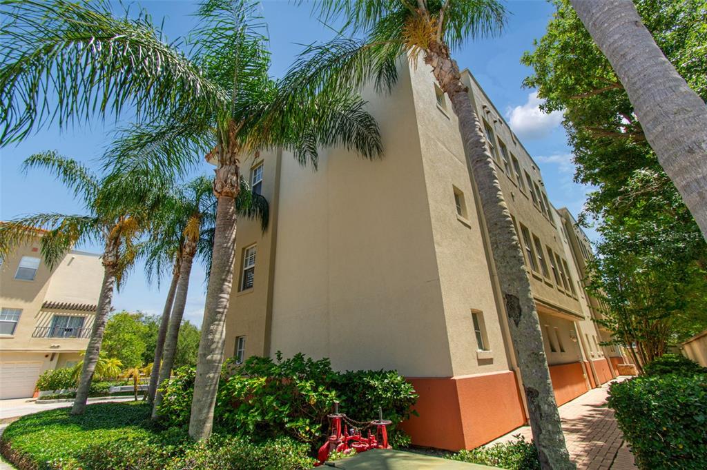 A low-angle view of a multi-story tan stucco apartment building with palm trees — 650 SIREN WIND LANE, CLEARWATER, FL