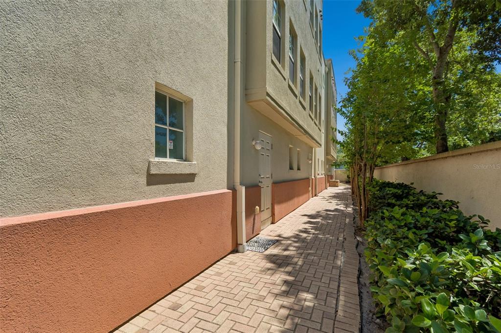 A paved walkway runs alongside the exterior wall of a multi-story building with landscaping — 650 SIREN WIND LANE, CLEARWATER, FL