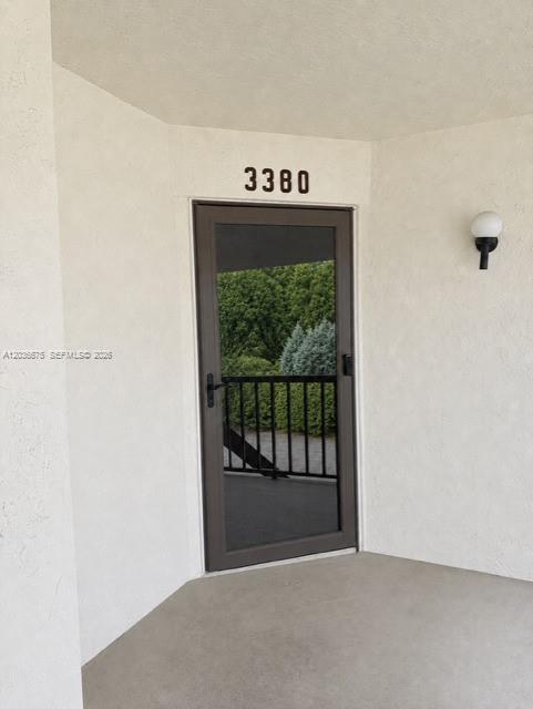 A view of a building entrance with a glass storm door and a wall-mounted light — 3380 Lucerne Park Dr # 4B, Green Acres FL 33467, GREEN ACRES, FL