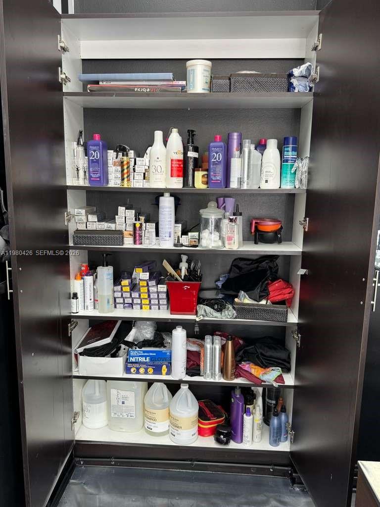 A tall, dark brown cabinet with open doors is filled with various hair salon supplies — Listing – Barbería Hialeah, Hialeah FL 33012, HIALEAH, FL