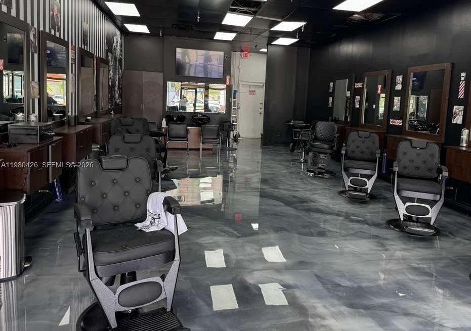A barbershop interior features multiple black styling chairs, dark cabinetry, and a glossy gray floor — Listing – Barbería Hialeah, Hialeah FL 33012, HIALEAH, FL