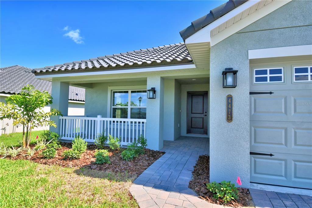 A light-colored house exterior features a covered porch, a paved walkway, and a garage door — 4964 TENNESSEE LAKE DRIVE, AUBURNDALE, FL