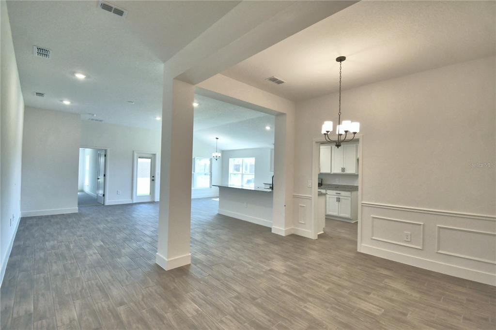An open-concept living area features gray wood-look tile flooring, white walls, and a kitchen — 4964 TENNESSEE LAKE DRIVE, AUBURNDALE, FL