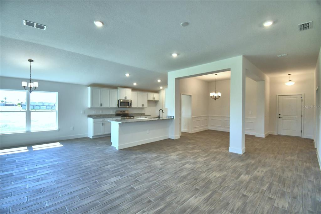 An open-concept kitchen and dining area with white cabinets, granite countertops, and wood-look tile flooring — 4964 TENNESSEE LAKE DRIVE, AUBURNDALE, FL