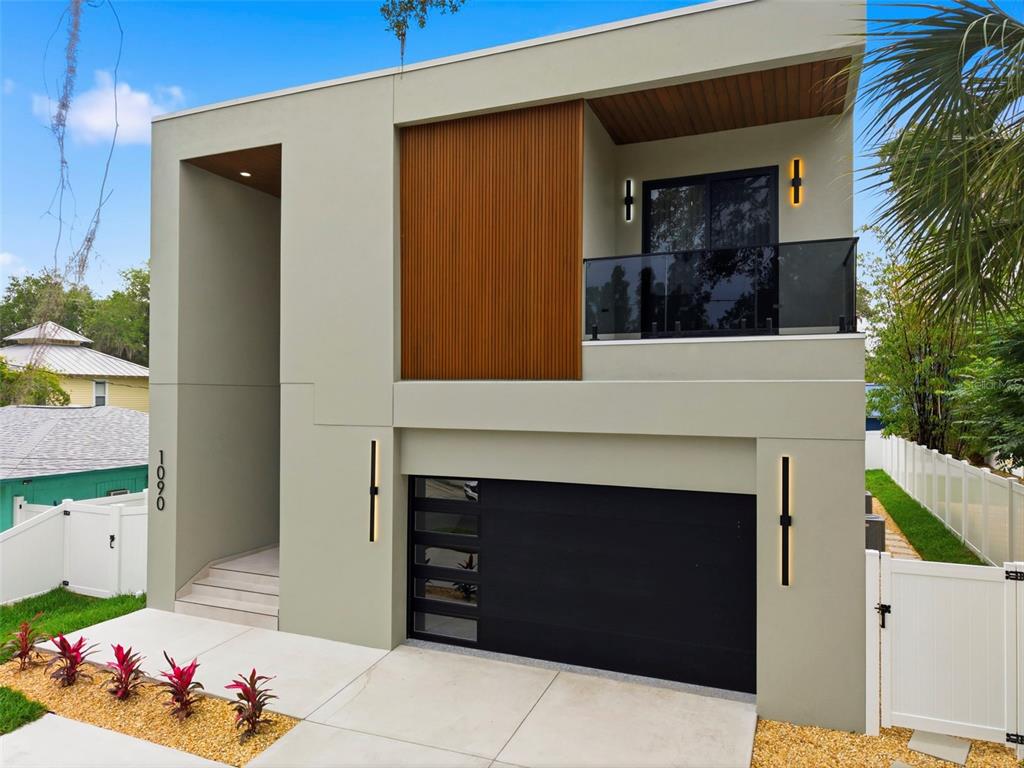 A modern two-story house features a black garage door, wood-slat siding, and a glass balcony — 1090 MAIN STREET, SAFETY HARBOR, FL