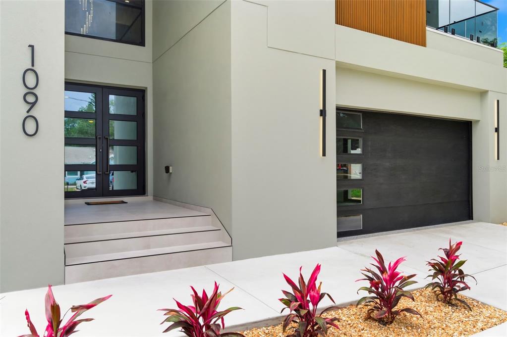 A modern house exterior features a dark front door, a garage, and tropical landscaping — 1090 MAIN STREET, SAFETY HARBOR, FL