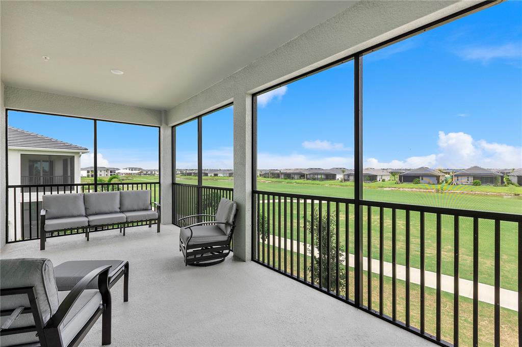 A covered balcony features gray patio furniture and a screened-in view of a grassy field — 15170 BLUFFTON LANE UNIT 1821, PUNTA GORDA, FL