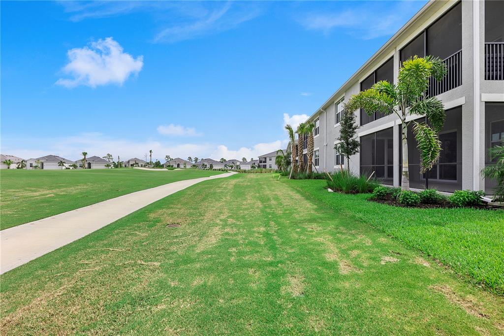 A paved path runs alongside a grassy lawn and a multi-story apartment building — 15170 BLUFFTON LANE UNIT 1821, PUNTA GORDA, FL