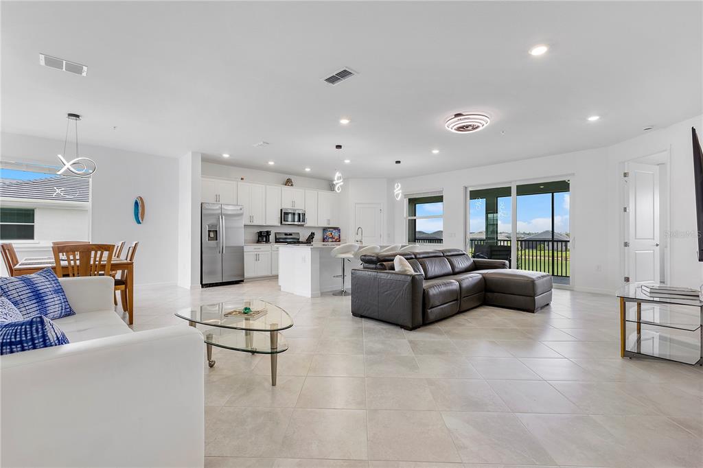 An open-concept living room and kitchen featuring white cabinetry, tile flooring, and a leather sectional — 15170 BLUFFTON LANE UNIT 1821, PUNTA GORDA, FL