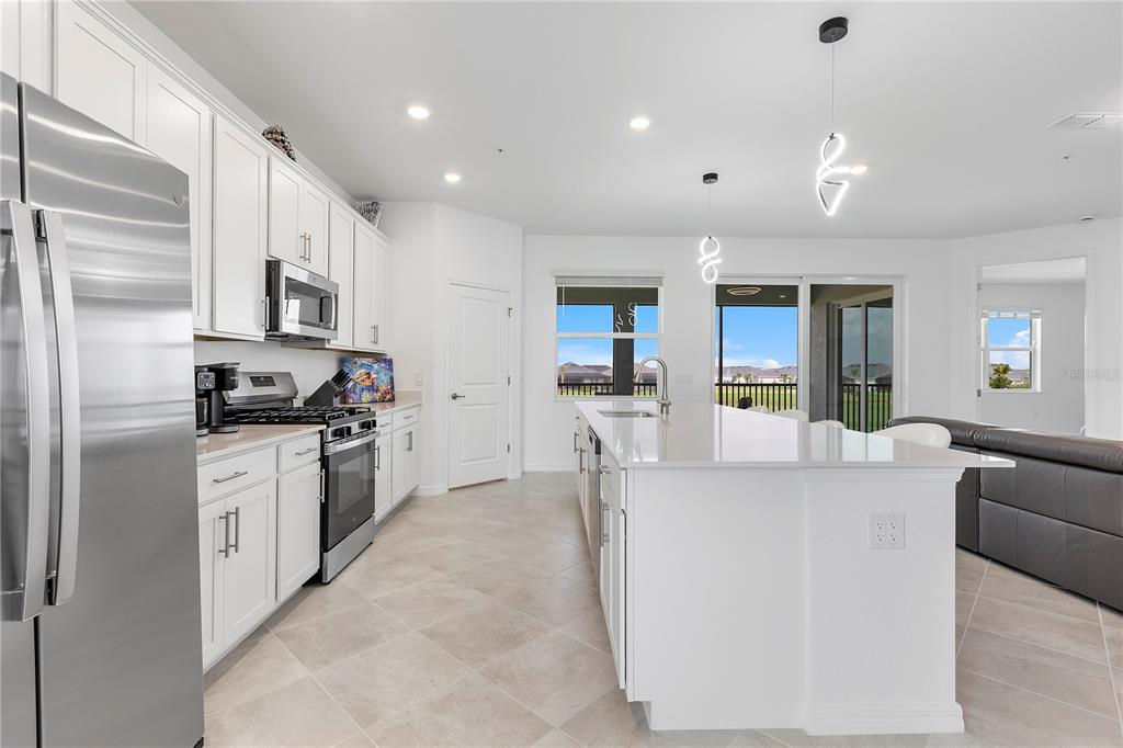 A modern white kitchen features a large island, stainless steel appliances, and tile flooring — 15170 BLUFFTON LANE UNIT 1821, PUNTA GORDA, FL