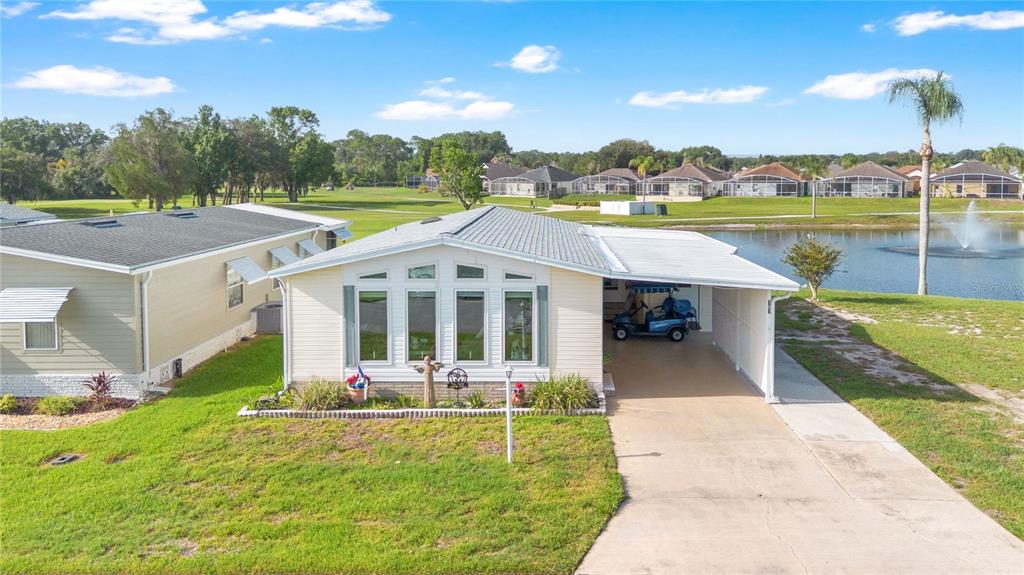 A single-story manufactured home with a carport, front windows, and a view of a pond — 707 POLO PARK EAST BOULEVARD, DAVENPORT, FL
