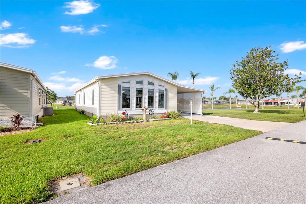 A light-colored manufactured home with a carport sits on a grassy lot under blue skies — 707 POLO PARK EAST BOULEVARD, DAVENPORT, FL