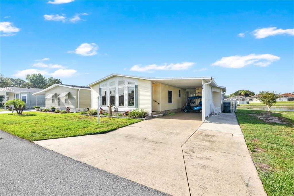 A light-yellow manufactured home features a concrete driveway, a carport, and a grassy yard — 707 POLO PARK EAST BOULEVARD, DAVENPORT, FL