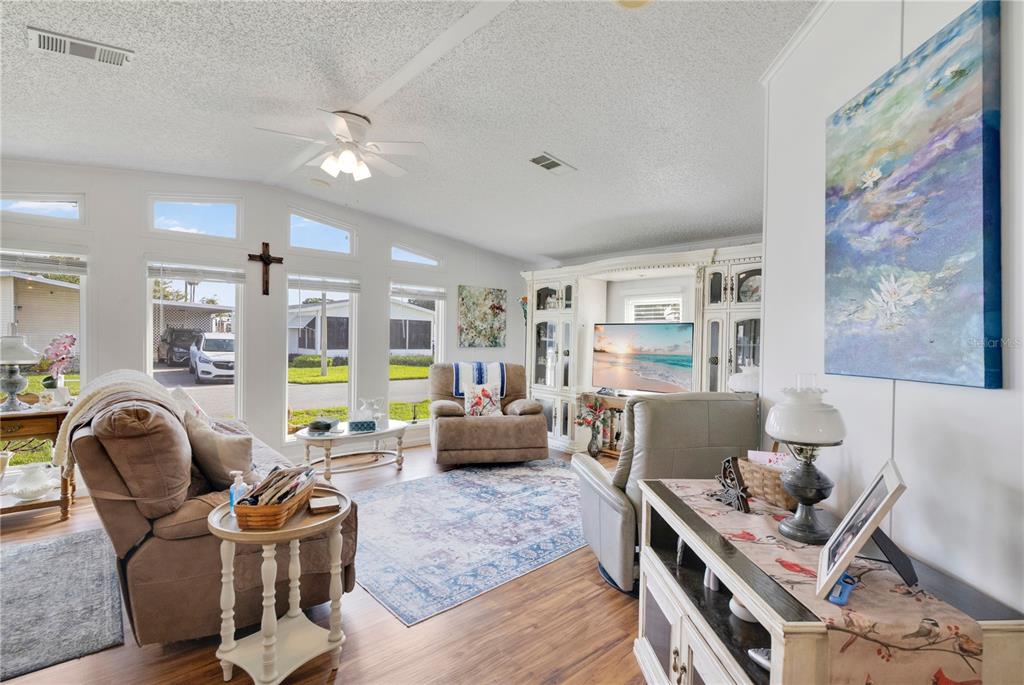 A living room features a ceiling fan, large windows, a television unit, and wood flooring — 707 POLO PARK EAST BOULEVARD, DAVENPORT, FL
