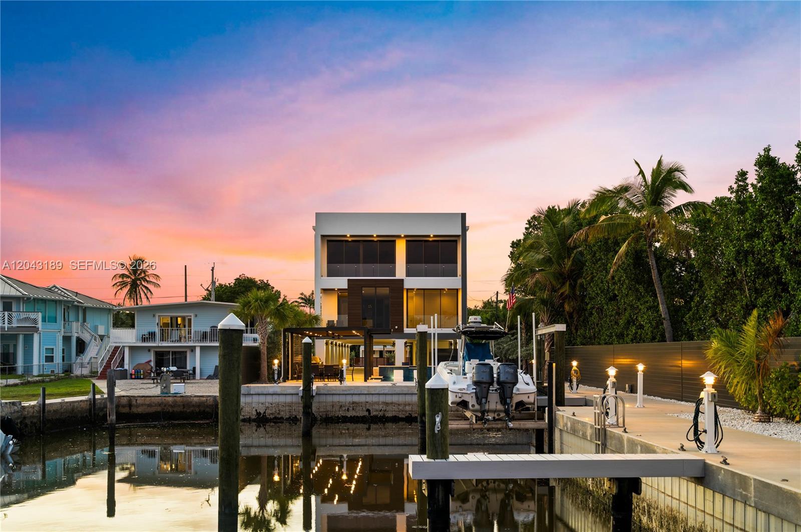 A modern three-story house sits on a canal with a boat docked at the pier — 16 Seaside Ave, Key Largo FL 33037, KEY LARGO, FL