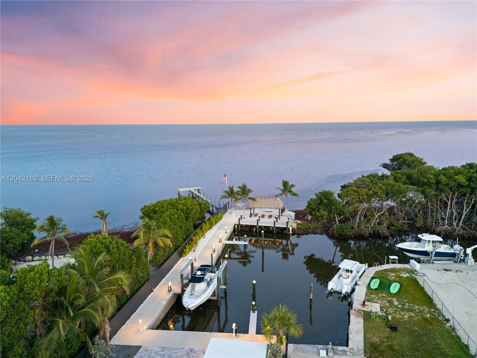 An aerial view shows a private boat dock and slip with a tiki hut at sunset — 16 Seaside Ave, Key Largo FL 33037, KEY LARGO, FL