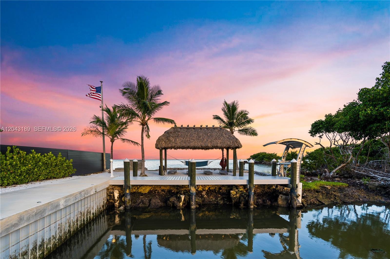 A wooden dock with a thatched-roof tiki hut sits by the water at sunset — 16 Seaside Ave, Key Largo FL 33037, KEY LARGO, FL
