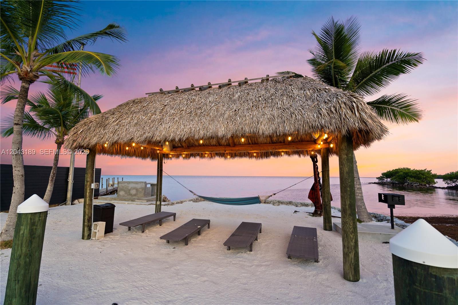 A thatched-roof tiki hut sits on a sandy beach with lounge chairs and a hammock — 16 Seaside Ave, Key Largo FL 33037, KEY LARGO, FL