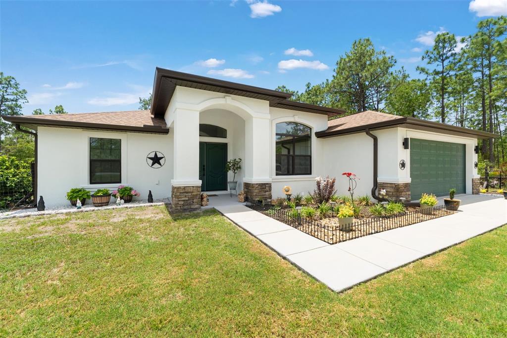 A single-story house with white stucco walls, a dark green garage door, and stone accents — 11096 WOOD OWL AVENUE, WEEKI WACHEE, FL