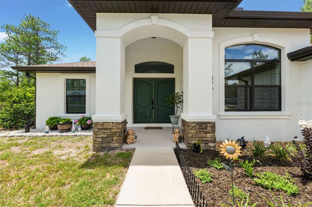 A front exterior view of a house with a stone-accented porch and green double doors — 11096 WOOD OWL AVENUE, WEEKI WACHEE, FL