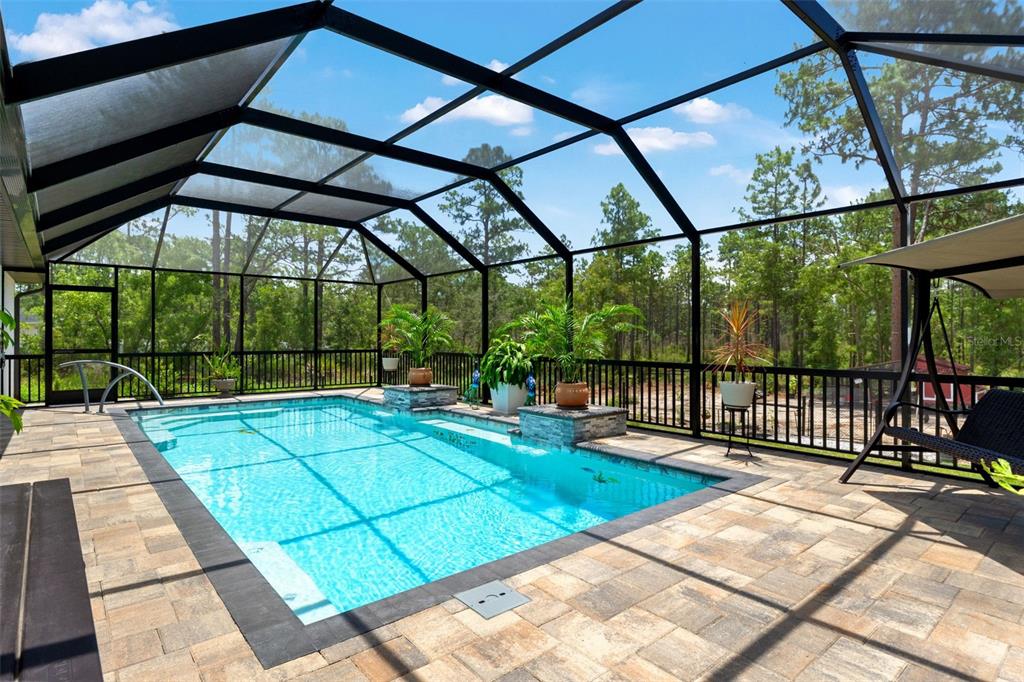 A rectangular swimming pool with a screened-in enclosure and stone paver deck — 11096 WOOD OWL AVENUE, WEEKI WACHEE, FL