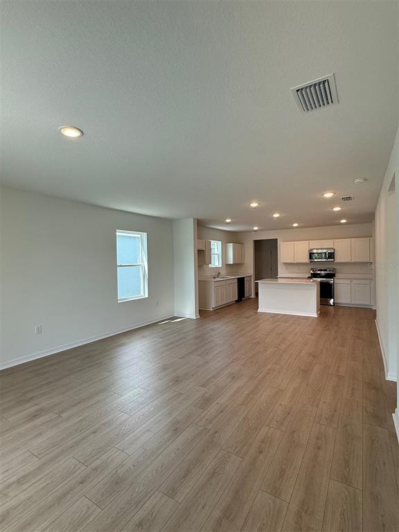 An open-concept kitchen and living area features light wood-look flooring and white cabinetry — 13025 RED DEER PLACE, PARRISH, FL