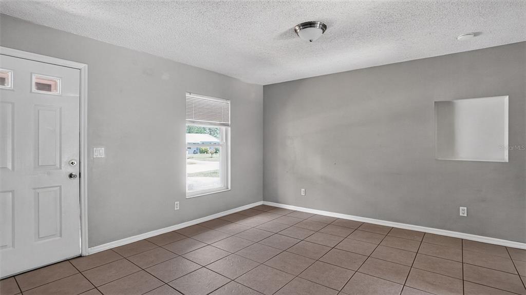 An empty room with gray walls, tile flooring, a white door, and a window — 1310 NE 20TH STREET, OCALA, FL