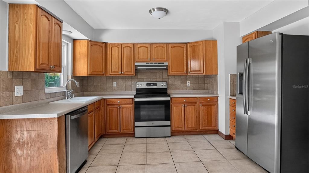 A kitchen with wood cabinets, stainless steel appliances, tile backsplash, and light-colored tile flooring — 1310 NE 20TH STREET, OCALA, FL