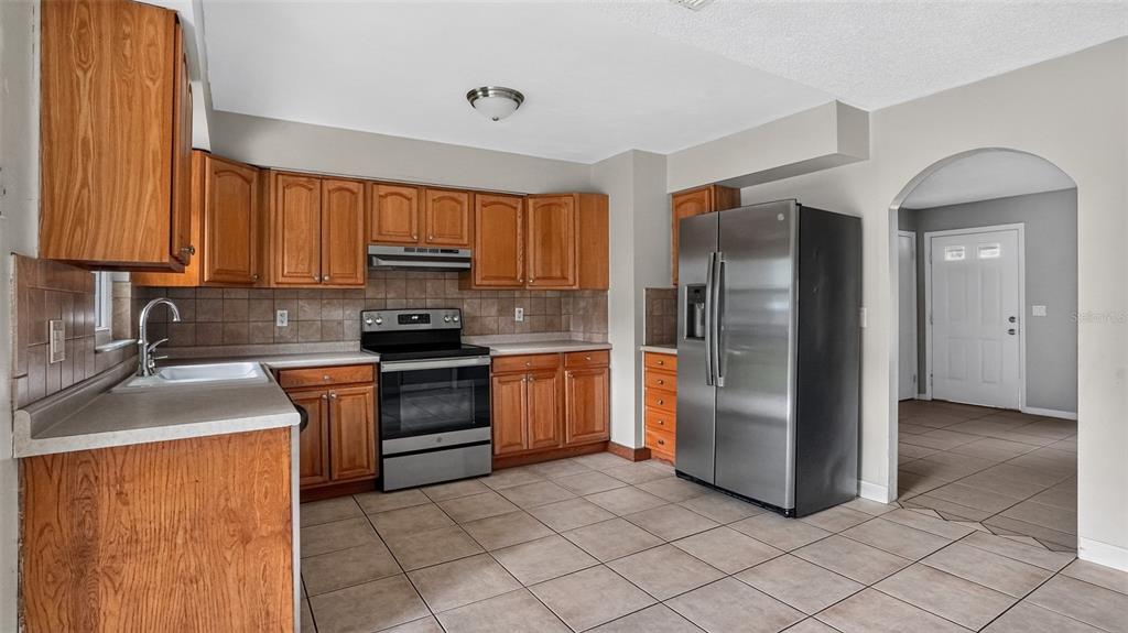 A kitchen features wood cabinets, stainless steel appliances, tile flooring, and a tiled backsplash — 1310 NE 20TH STREET, OCALA, FL