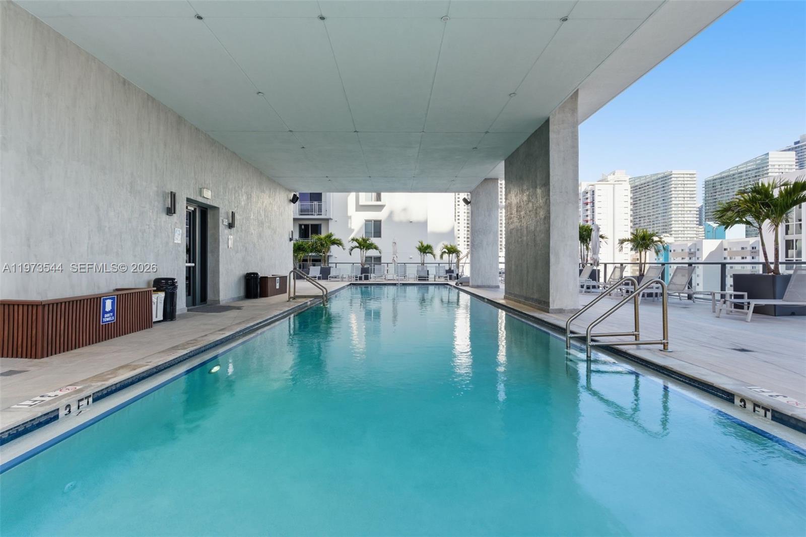A rectangular swimming pool is situated on a rooftop terrace surrounded by lounge chairs — 229 SW 9th St # 407, Miami FL 33130, MIAMI, FL