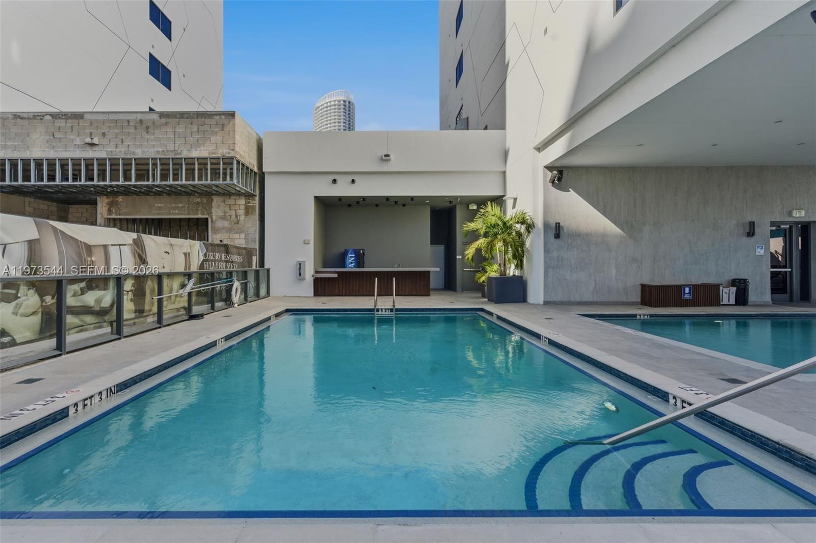An outdoor swimming pool area features a bar, lounge seating, and modern building architecture — 229 SW 9th St # 407, Miami FL 33130, MIAMI, FL