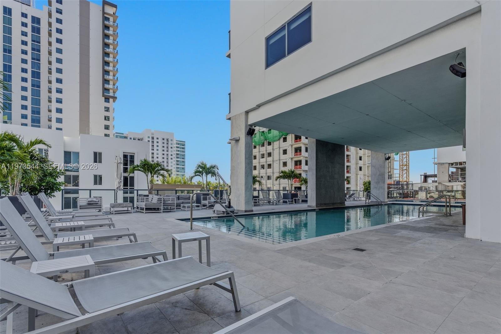 A swimming pool sits on a paved terrace with lounge chairs under a building overhang — 229 SW 9th St # 407, Miami FL 33130, MIAMI, FL