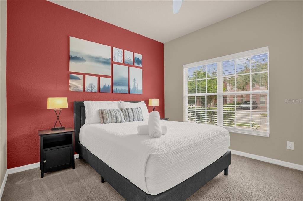 A bedroom features a bed with white bedding against a red accent wall with artwork — 2344 CARAVELLE CIRCLE, KISSIMMEE, FL