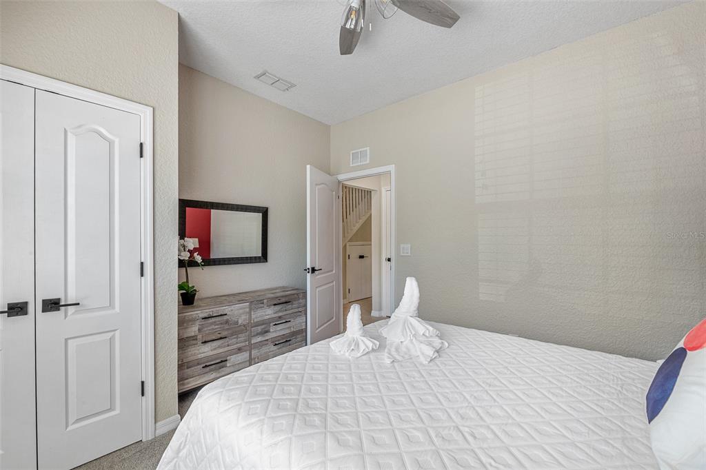 A bedroom features a white bed with towel swans, a wooden dresser, and an open doorway — 2344 CARAVELLE CIRCLE, KISSIMMEE, FL