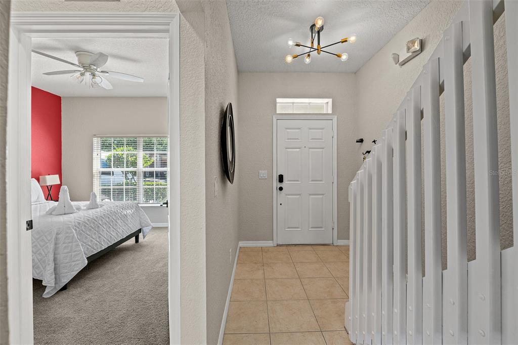 A tiled entryway leads to a bedroom with a red accent wall and a staircase — 2344 CARAVELLE CIRCLE, KISSIMMEE, FL