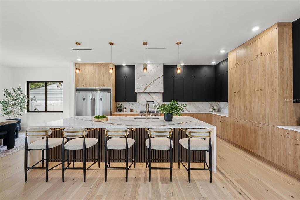 A modern kitchen features a marble island, wood cabinetry, black upper cabinets, and bar stools — 12870 N ARMENIA AVENUE, TAMPA, FL