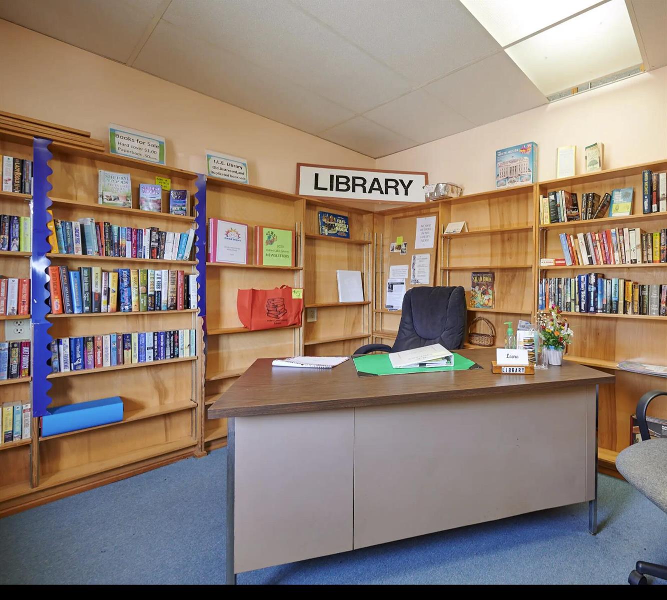 A library room features wooden bookshelves, a central desk, and a blue carpeted floor — 1015 Calendula Drive, FL 33855, FL